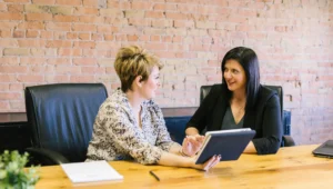 Two female HR professionals sitting down in an office and discussing the use of HR tools.