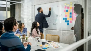 A business analyst in an interview, carrying out a live demonstration of how to solve a problem. He is writing on a whiteboard in front of a panel of interviewers.